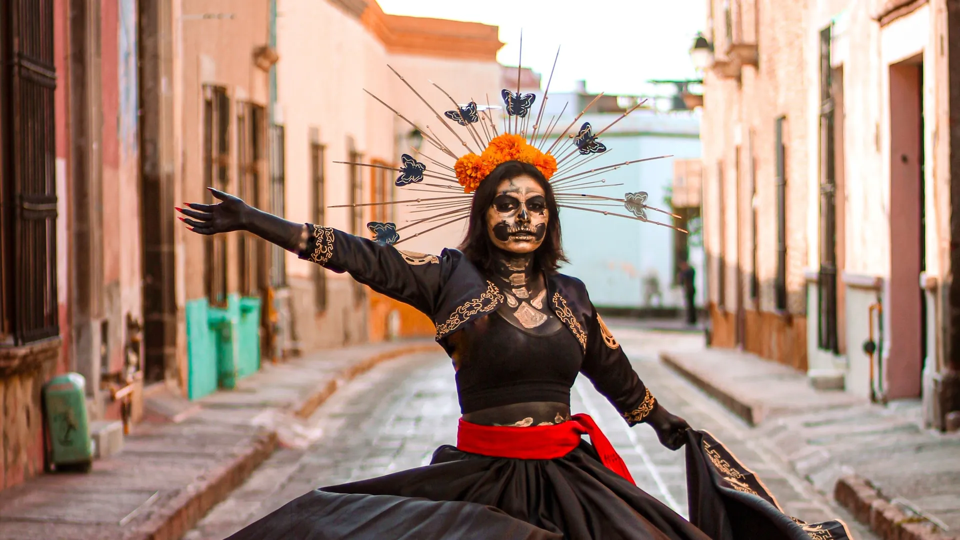 A woman dressed as La Catrina, with a marigold crown, dancing on a cobblestone street